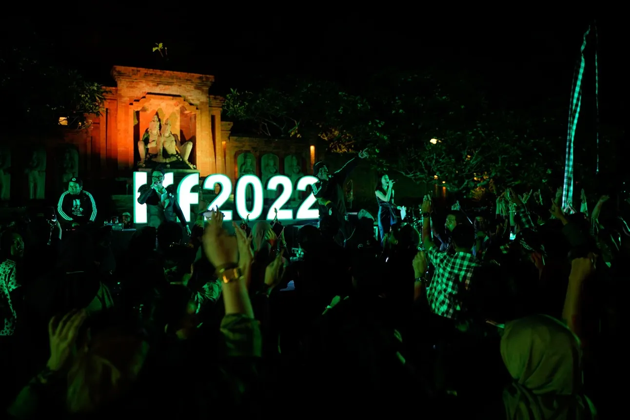IFF 2022 outing in Bali: guests raising their hands in front of the glowing IFF 2022 sign at night