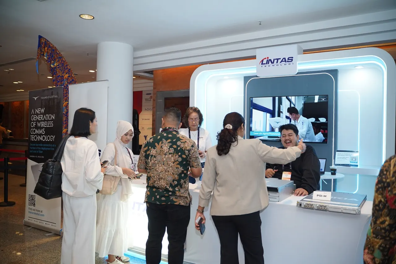 Visitors queuing at the Lintas Teknologi booth counter while a staff member laughs with a guest