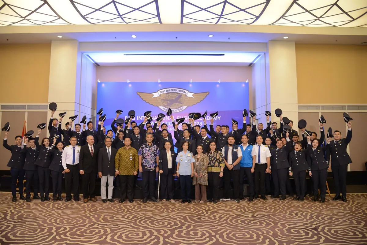 Bali International Flight Academy graduates throwing their caps in the air with guests on stage